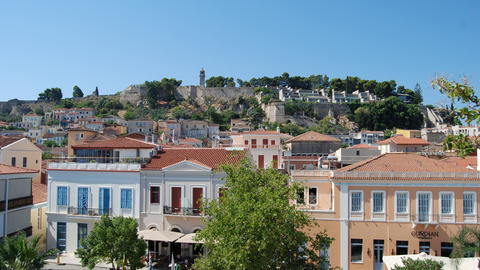 Ιστορικό φρούριο στην κορυφή λόφου με θέα σε πόλη με πολύχρωμα κτίρια και κεραμοσκεπές κάτω από καταγάλανο ουρανό.