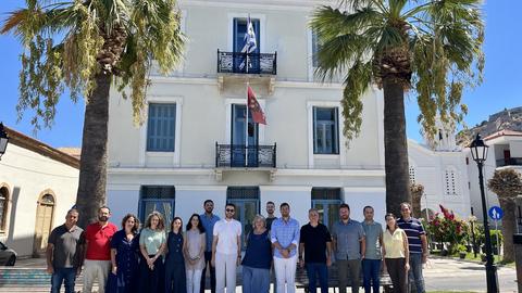 Ομαδική φωτογραφία των συμμετεχόντων και των συμμετεχουσών έξω από το κτίριο του ΚΕΣ στο Ναύπλιο, ανάμεσα σε δύο φοίνικες.