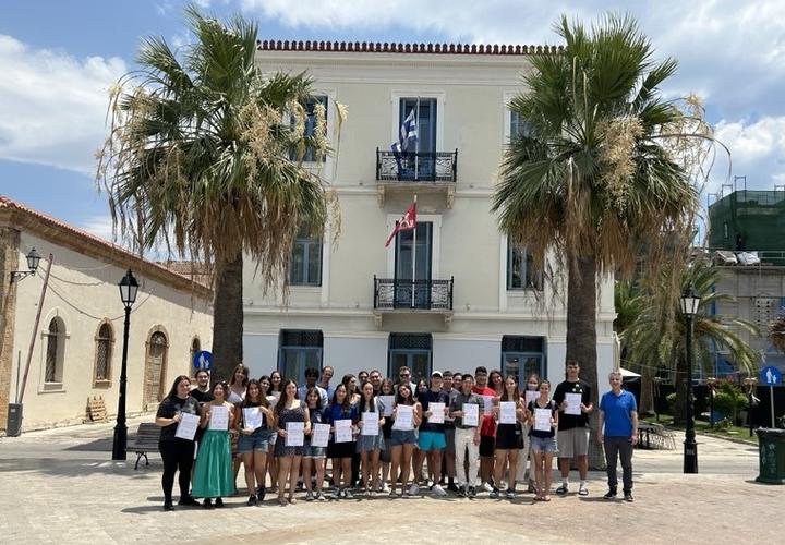 Ομάδα νεαρών συμμετεχόντων, μαζί με τη διδακτική ομάδα του HSSP 2024, στέκονται μπροστά από το κτίριο που στεγάζει το ΚΕΣ στην πλατεία Φιλελλήνων. Όλοι τους κρατούν με υπερηφάνεια τα διπλώματα ολοκλήρωσης του προγράμματος.