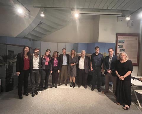 10άτομα στέκονται και χαμογελούν στην κάμερα σε αίθουσα για διαλέξεις.