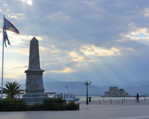 A town square with a obelisk-shaped monument that receives a few sunrays on a cloudy day.