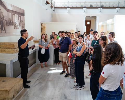 Ομάδα ανθρώπων διάφορων ηλικιών σε μουσειακό χώρο ακούει με προσοχή τον καθηγητή Stocking να μιλά και να χειρονομεί με τα χέρια του.